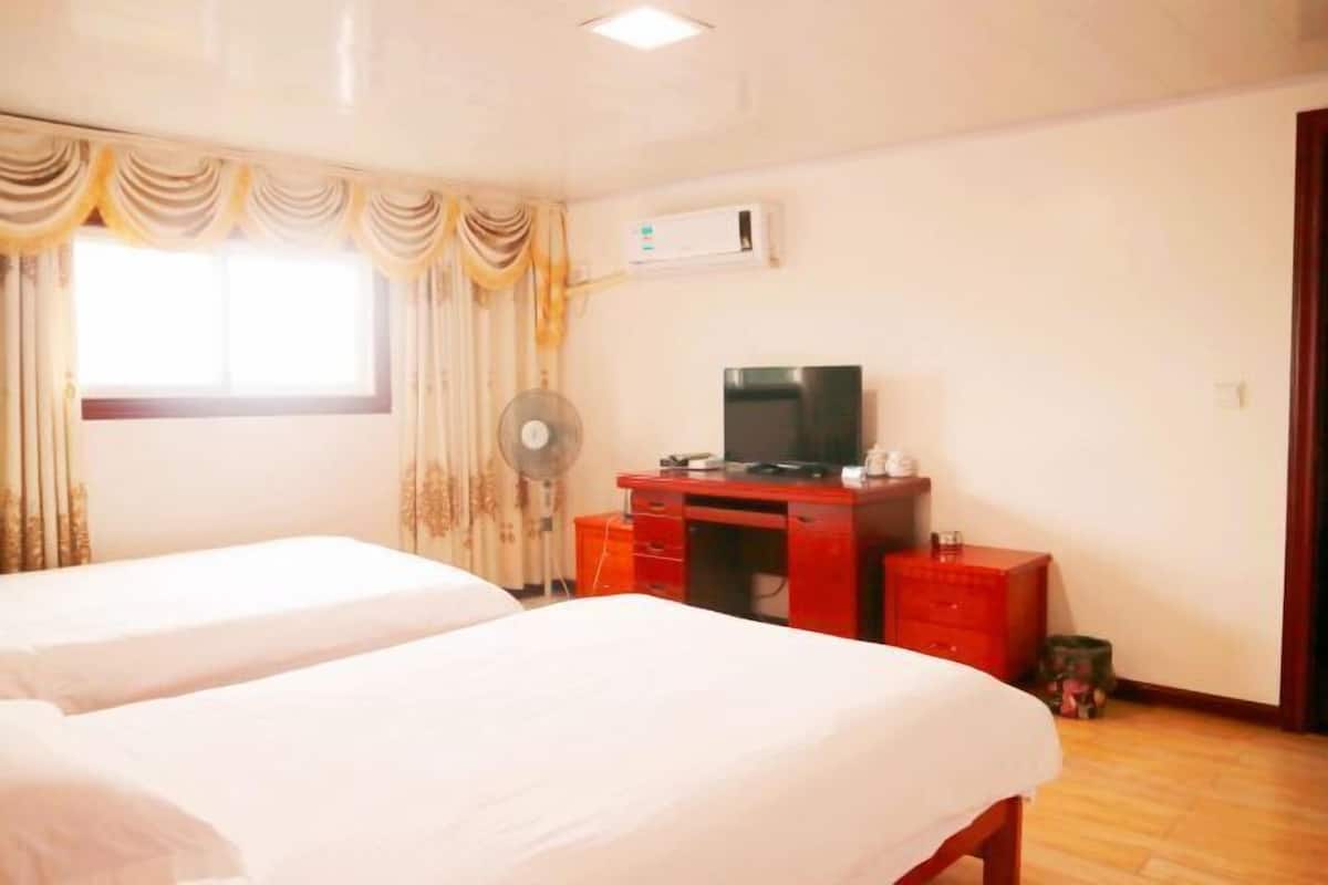 A hotel room with two beds, a TV, a desk, and a fan.