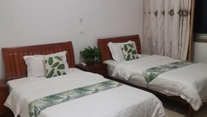 Habitación de hotel con dos camas individuales, cada una con cabecera de madera, ropa de cama blanca y almohada con estampado de hojas verdes.