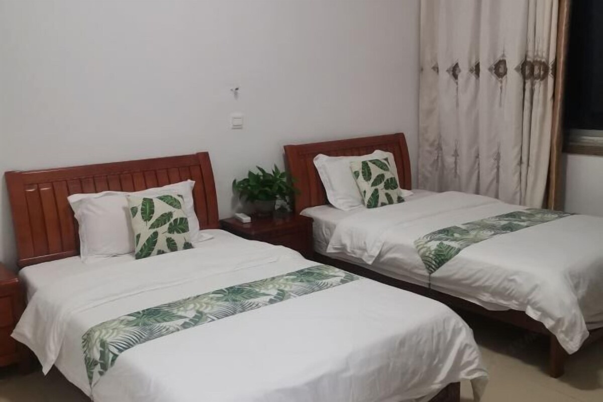 Habitación de hotel con dos camas individuales, cada una con cabecera de madera, ropa de cama blanca y almohada con estampado de hojas verdes.