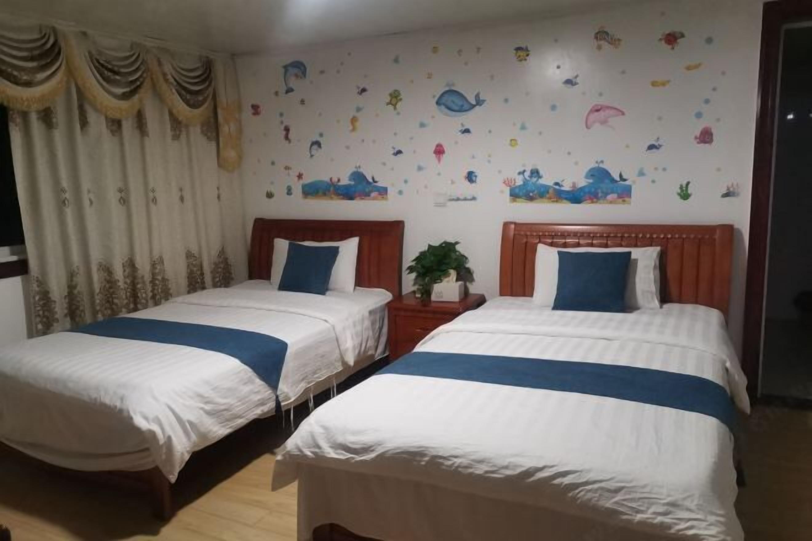 Habitación de hotel con dos camas, una mesita de noche, una planta en maceta y una pared decorada con pegatinas de animales.