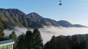 Un paisaje montañoso con un teleférico, colinas boscosas y un edificio de techo azul.