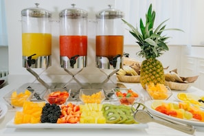 Un buffet de petit-déjeuner avec des fruits, des distributeurs de jus et un ananas.