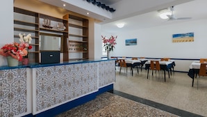 Un espace d’accueil avec un comptoir décoré, une maquette de bateau et un coin repas avec des tables et des chaises.
