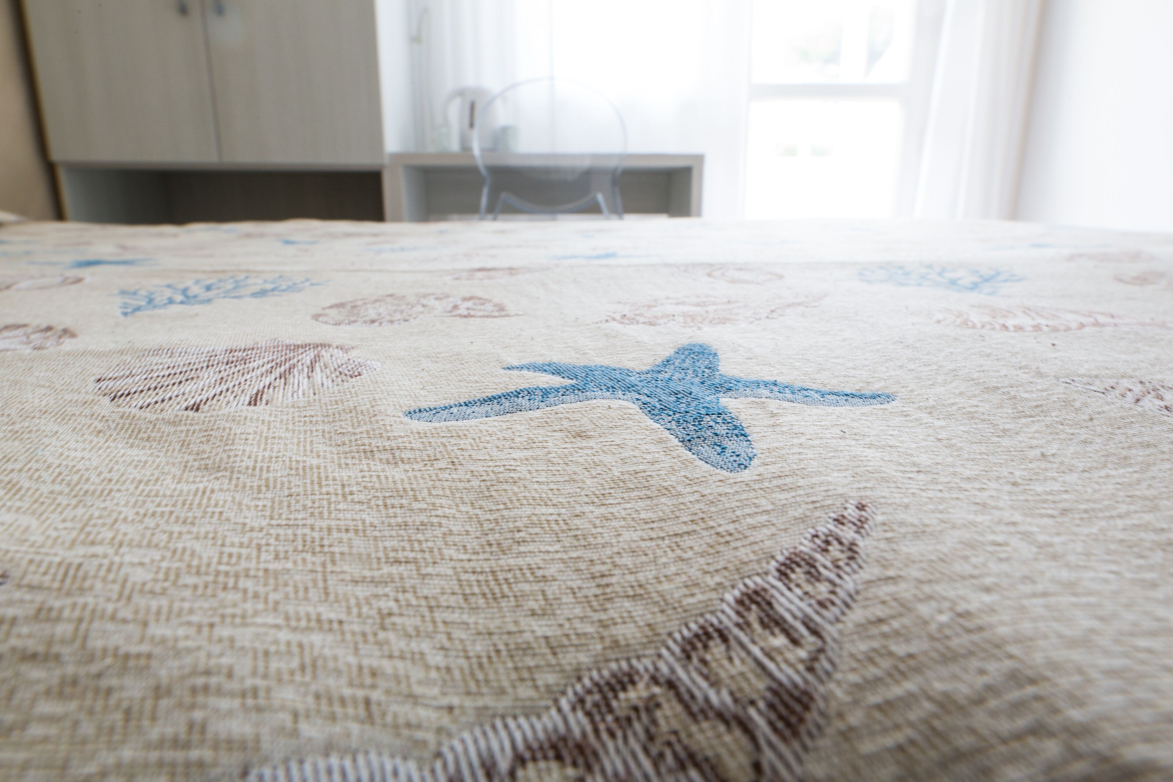 A bed with a beige and blue patterned bedspread, a wooden headboard, and a window with curtains in the background.
