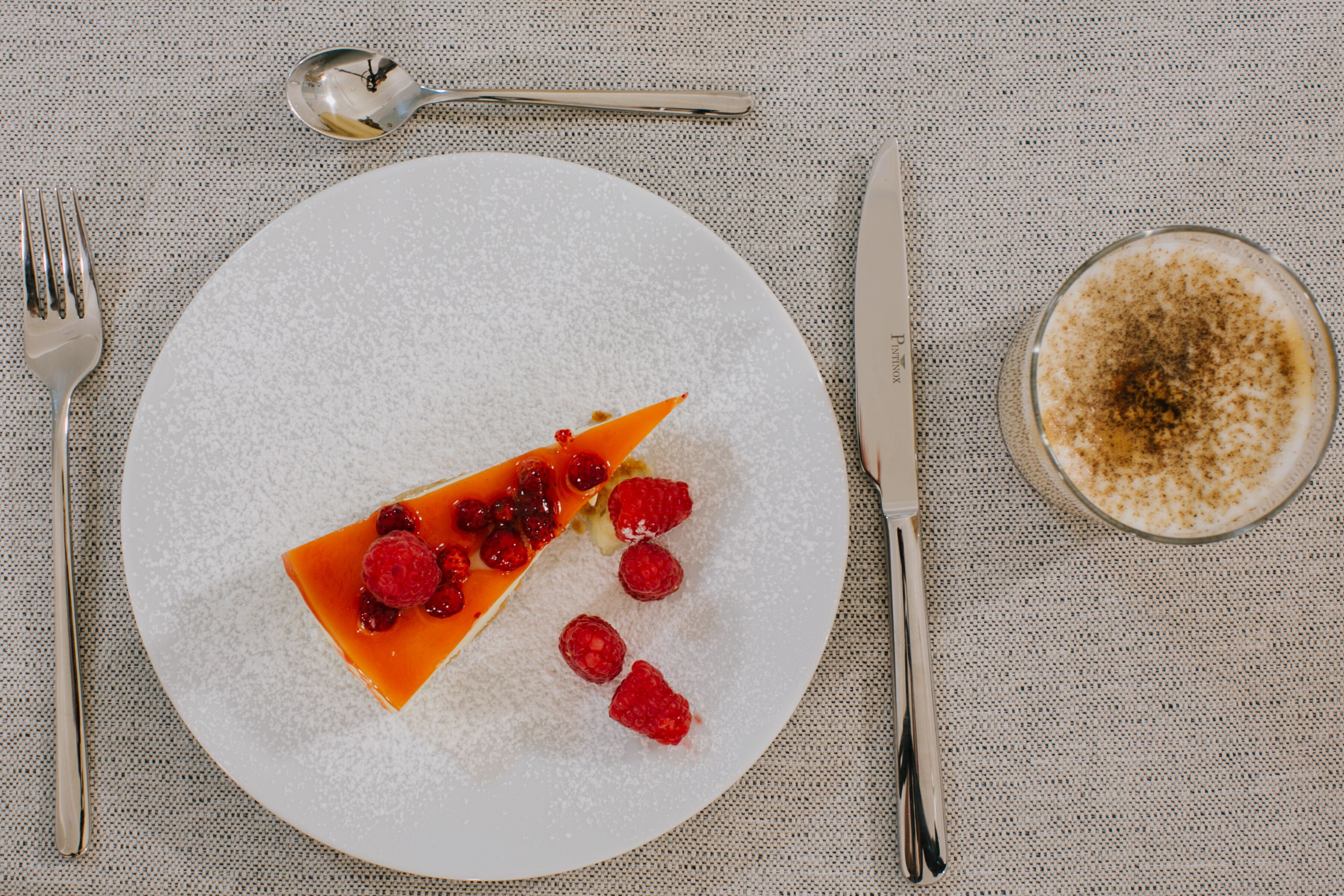 A dessert plate with a slice of cake, raspberries, and powdered sugar.