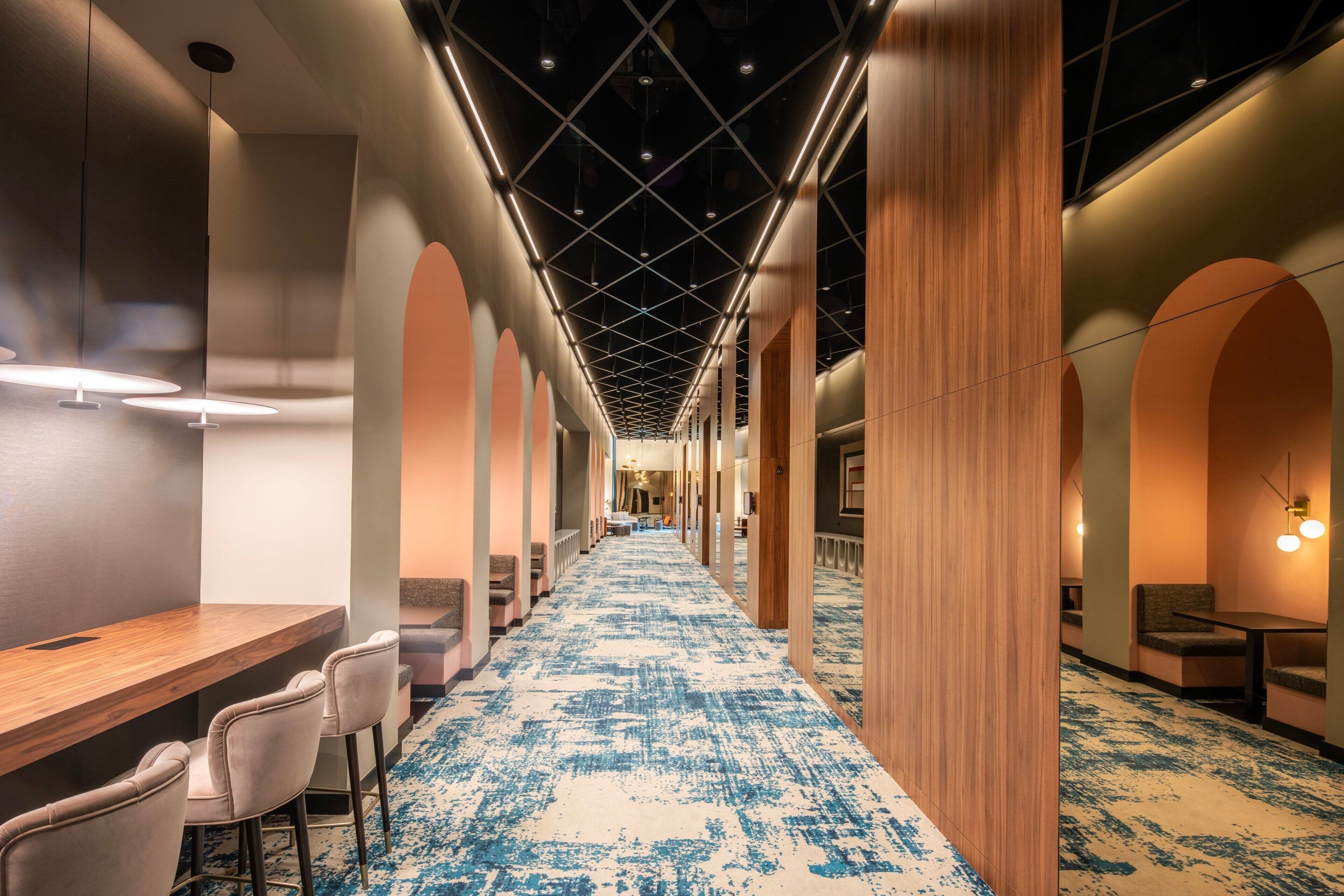 Un couloir d’hôtel avec un tapis à motifs bleus, des piliers en bois et des tables avec des chaises.