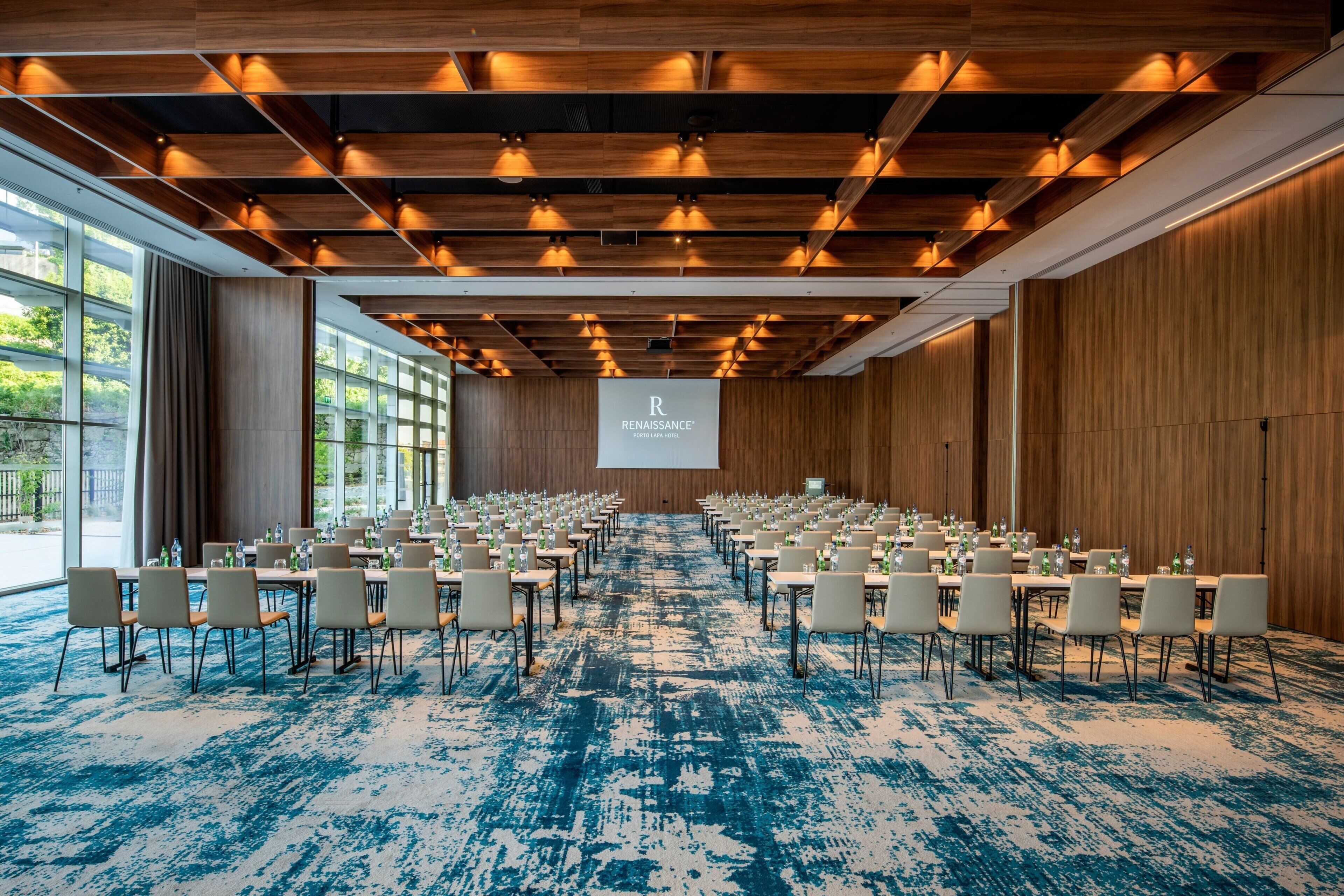 A conference room with rows of tables and chairs, a large screen at the front, and wooden paneling on the walls.