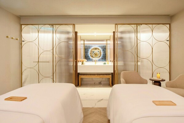 A hotel room with two beds, a wooden bench, a small table with a candle, and a decorative mirror with a blue and gold design.