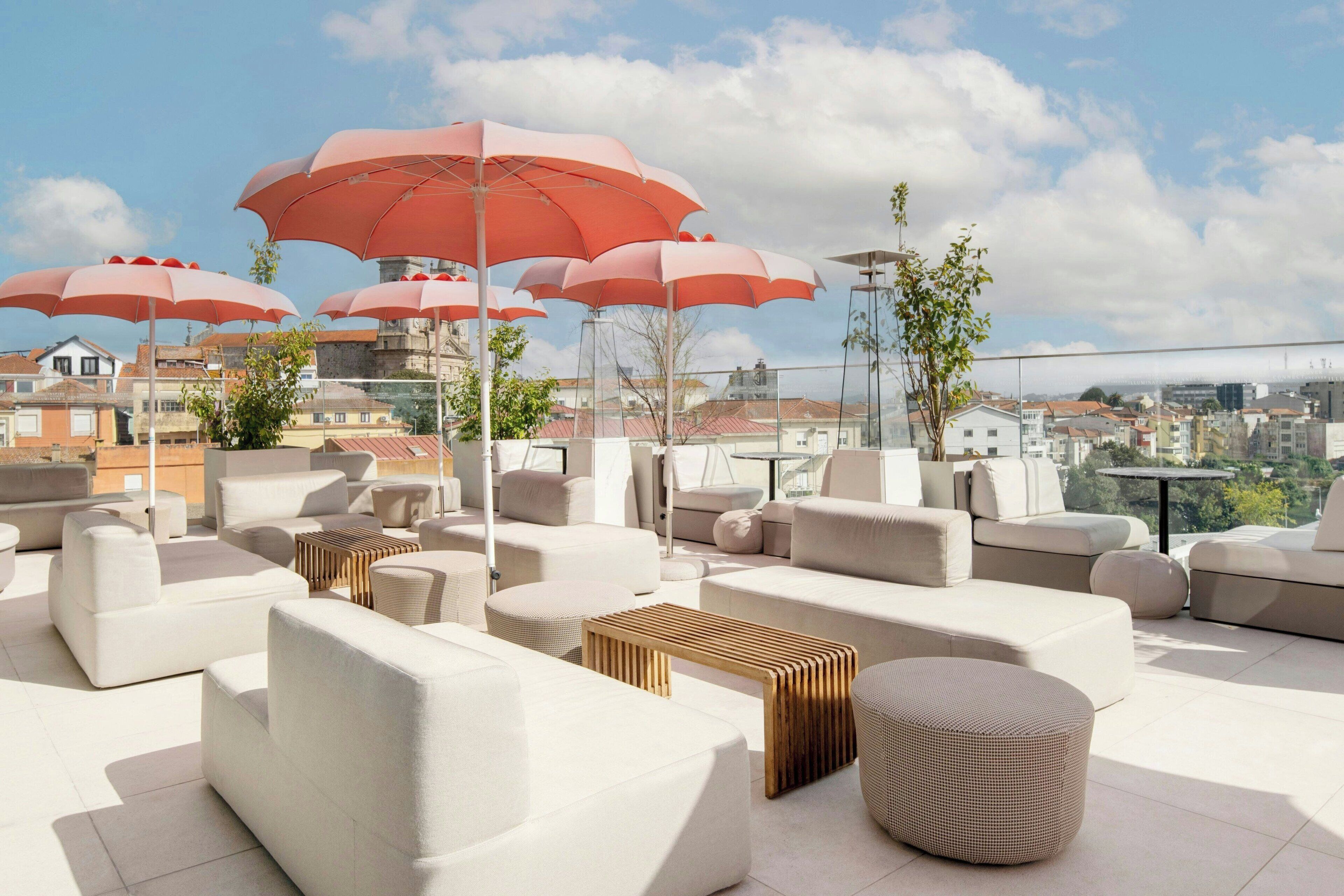 Un salon sur le toit doté de plusieurs espaces de détente, notamment des canapés et des poufs, ainsi que de plusieurs grands parasols rouges qui offrent de l’ombre.