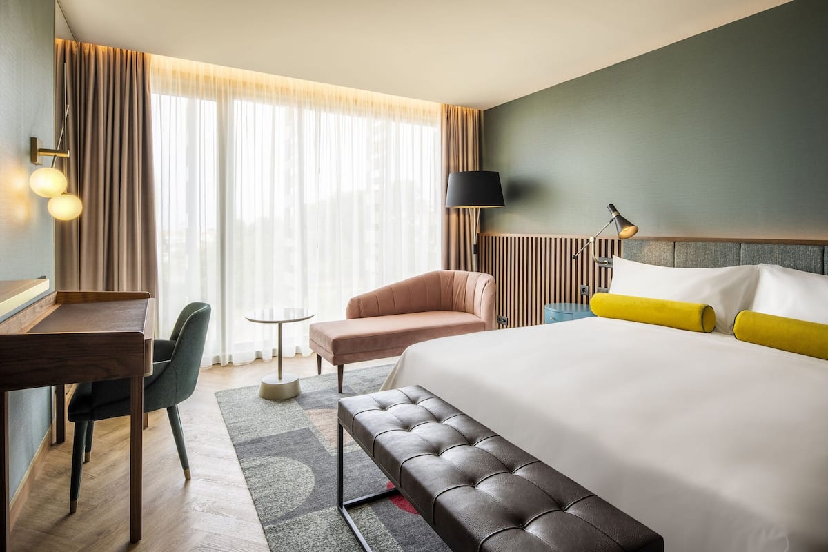 A hotel room with a large bed, a desk, a chair, and a small table.