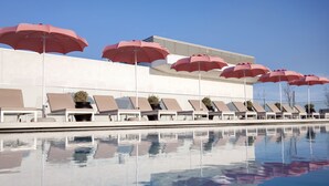 Zona de piscina con tumbonas y sombrillas rojas, reflejada en el agua.