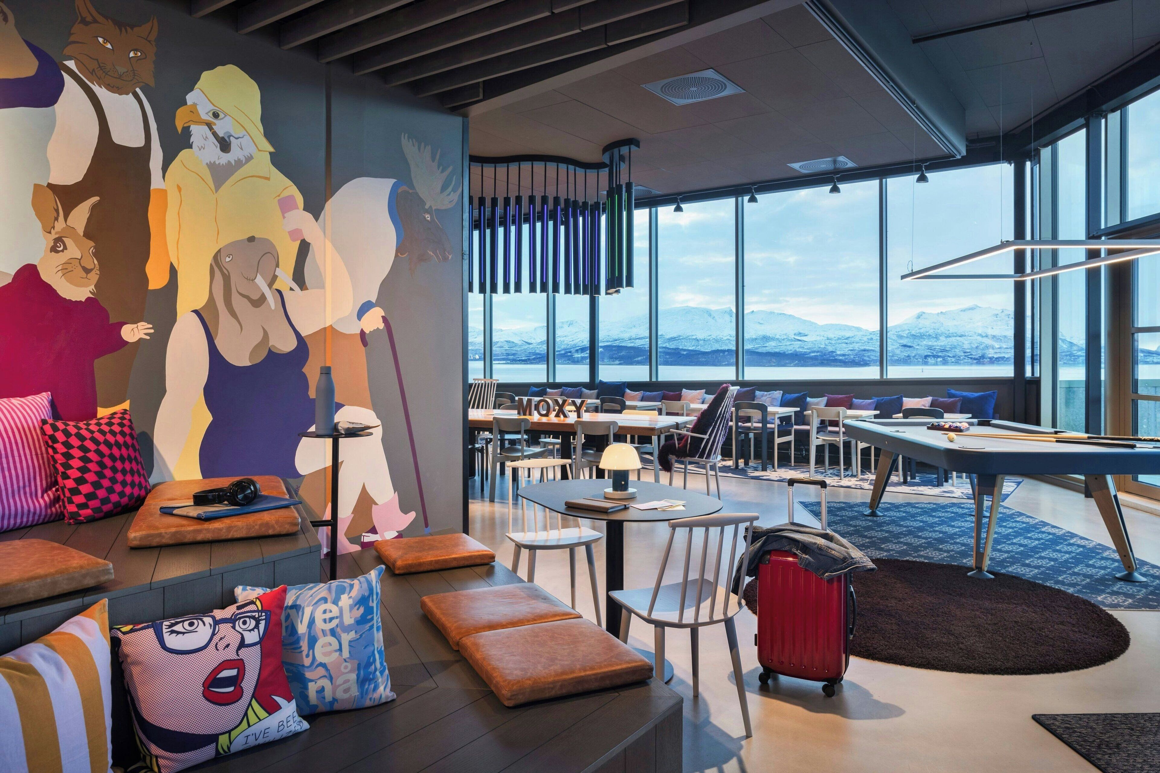A modern lounge area with seating, a pool table, and a mural of various animals.