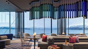 A modern lounge with a large window overlooking a snowy landscape, featuring a grey sofa, chairs, and a unique hanging light fixture.