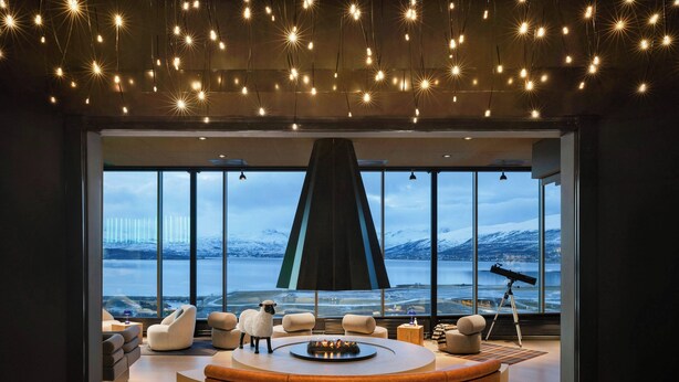 A modern living room with a circular seating area, large windows with a view of a snowy landscape, and a telescope on a tripod.