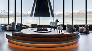 A modern interior with a circular seating area, a fireplace, and a view of a lake and mountains.