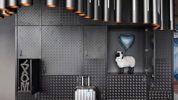 A modern hotel lobby with metallic ceiling fixtures, a heart-shaped balloon, a plush sheep decoration, and a suitcase on the floor.