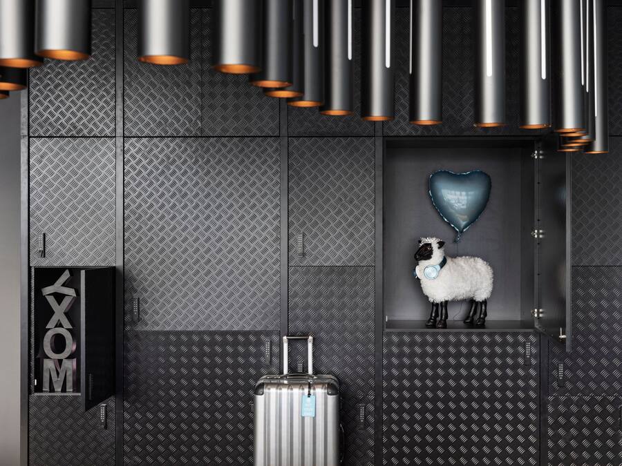A modern hotel lobby with metallic ceiling fixtures, a heart-shaped balloon, a plush sheep decoration, and a suitcase on the floor.
