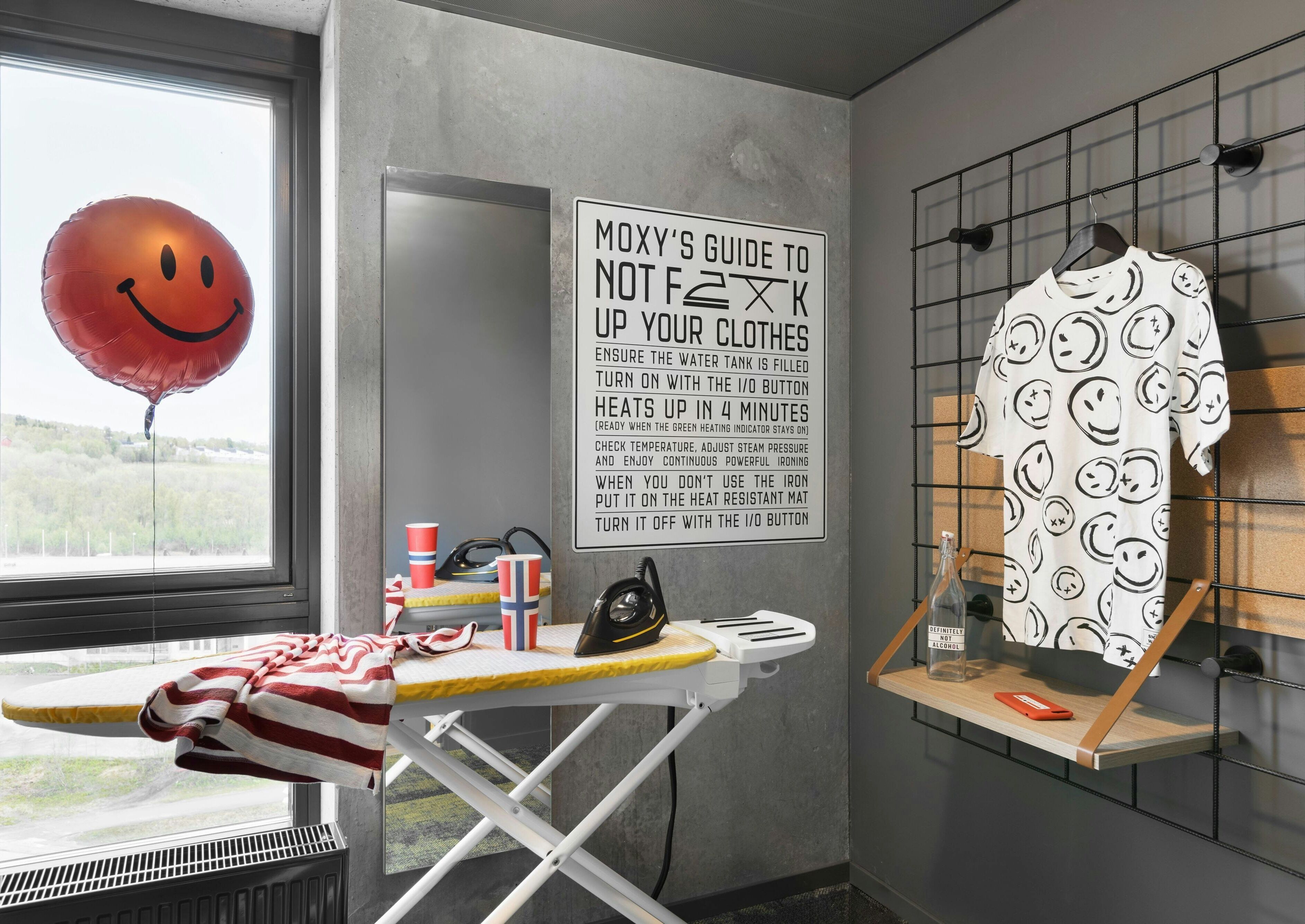 A laundry area with a drying rack, iron, and a wall-mounted ironing board. A sign provides instructions for using the iron.