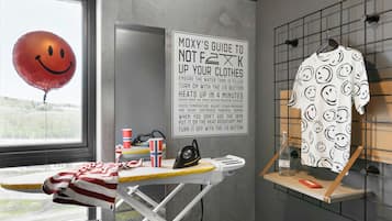 A laundry area with a drying rack, iron, and a wall-mounted ironing board. A sign provides instructions for using the iron.