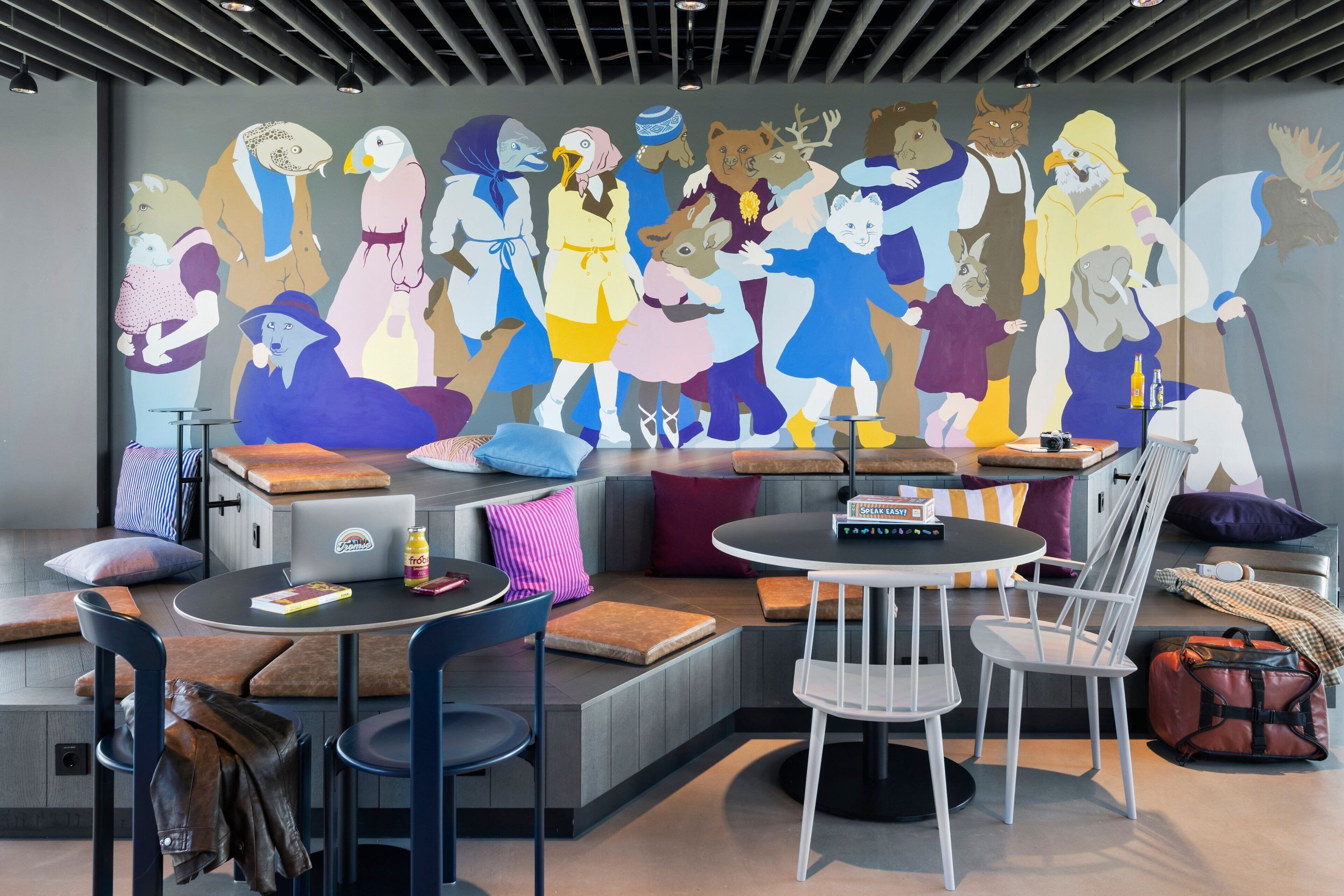 A modern lounge area with seating, a mural, and a table with a laptop and a bottle.
