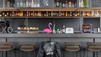 Un bar avec des étagères remplies de bouteilles d'alcool de toutes sortes, un panneau au néon représentant un flamant rose et un autre panneau au néon sur lequel on peut lire : « L’AMOUR TRIOMPHE ».