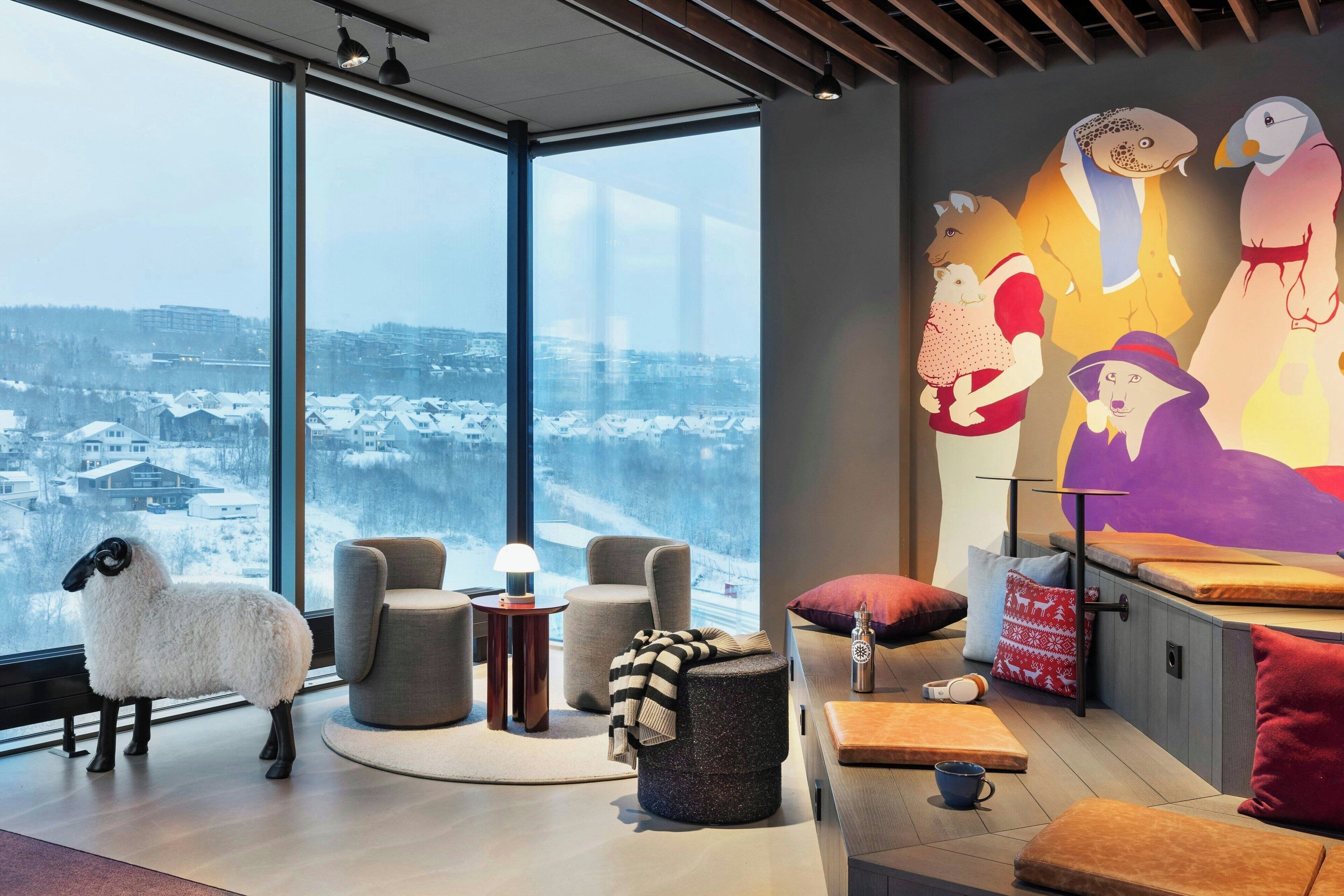 A modern interior with a large window overlooking a snowy landscape, a cozy seating area, and a colorful mural on the wall.