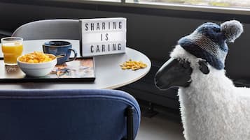 A cozy room with a table set for breakfast, a bowl of cereal, a cup, and a tray with cereal and a glass of orange juice. A sign on the wall reads "SHARING IS CARING."