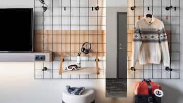 Una habitación moderna con una televisión, un estante con auriculares y una botella de agua, un suéter colgado, un pequeño otomaní y un bolso.