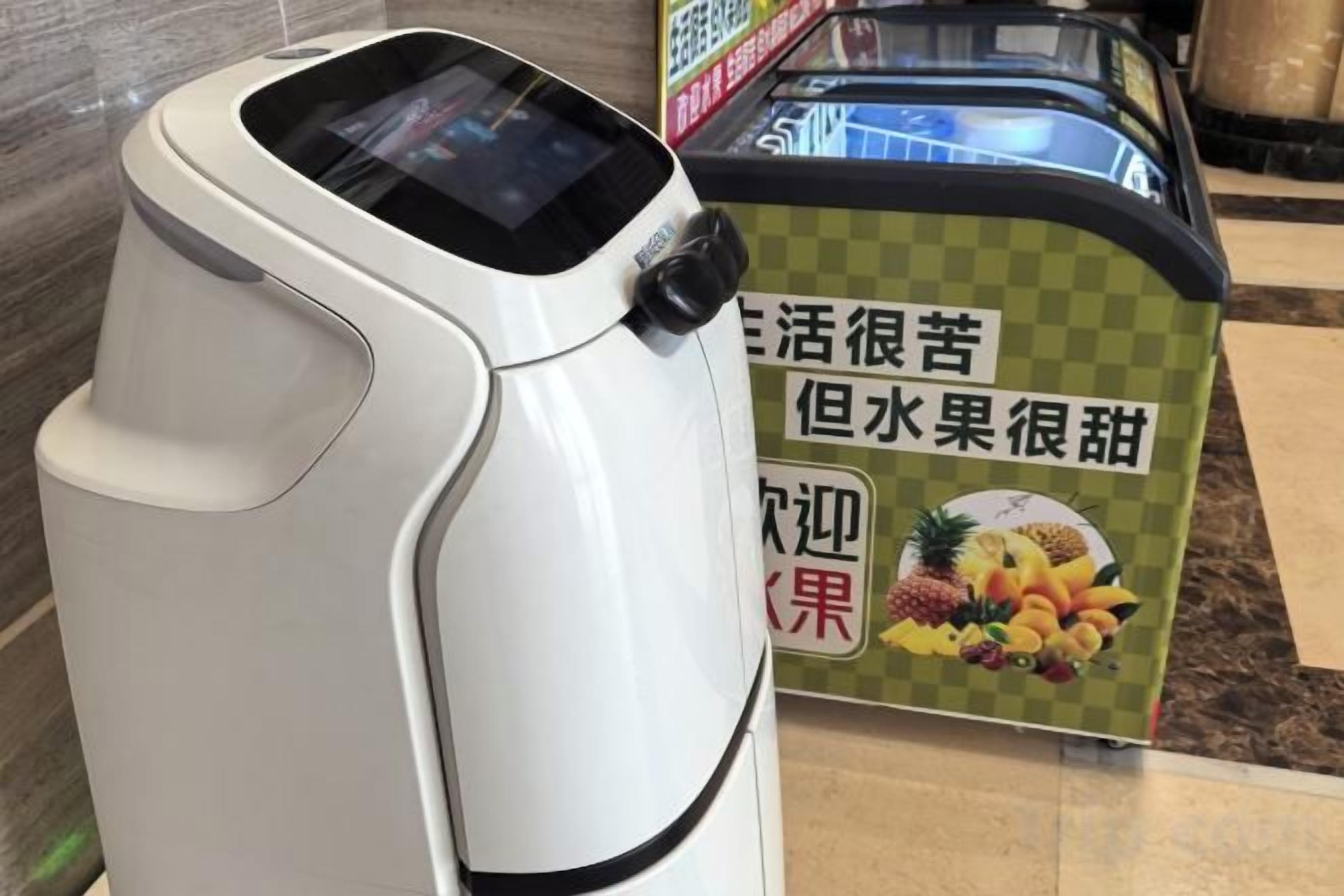 En dryckesautomat med självbetjäning, utrustad med en digital display och en reklamskylt med bilder av frukt.