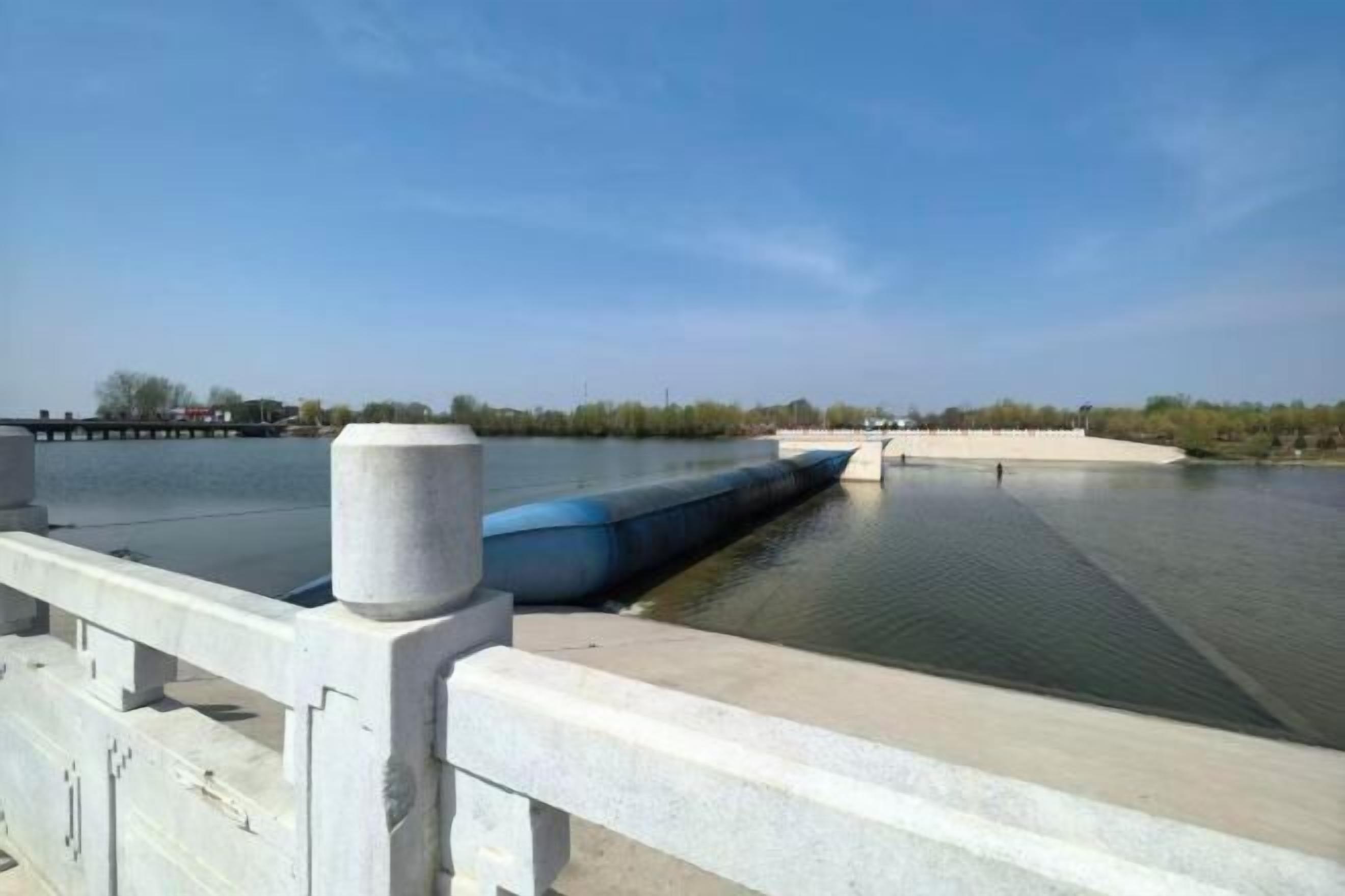 A bridge with a water channel, a clear sky, and distant trees.