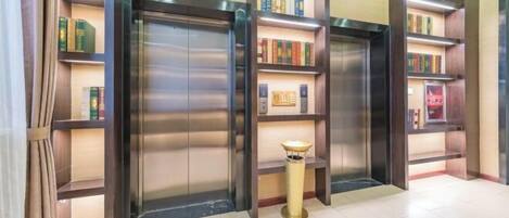 A lobby with a modern design, featuring a central elevator surrounded by bookshelves.