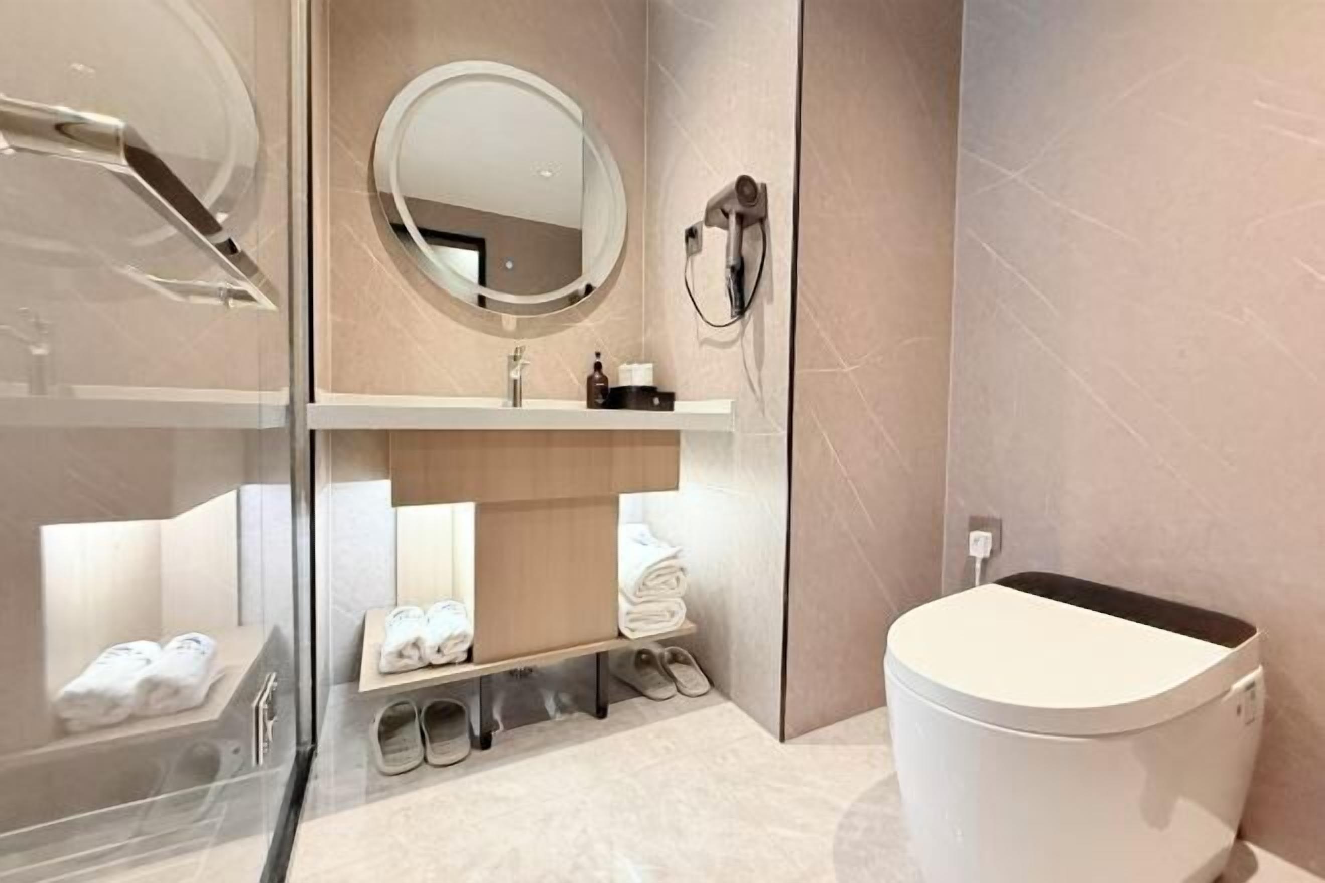 A modern bathroom with a glass shower enclosure, a round mirror, a toilet, and a towel rack with folded towels.