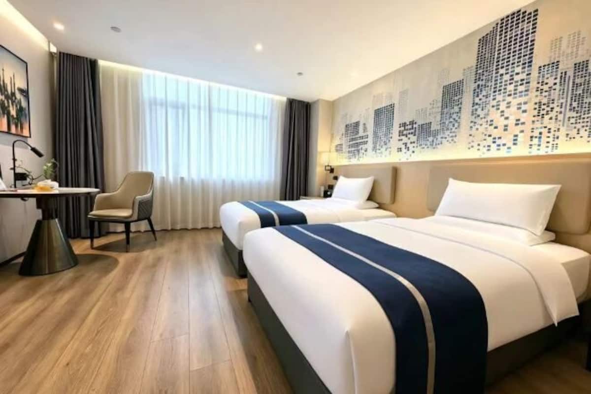 Habitación de hotel con dos camas, un escritorio, una silla y un ventanal con cortinas.