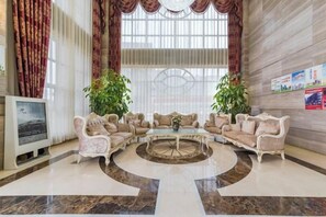 A lobby with a round coffee table, sofas, a TV, and two potted plants. - Tianyi Mingdu Mansion (Longyao County)