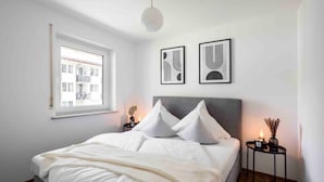 A bedroom with a bed, two bedside tables, a window, and two wall-mounted abstract art pieces. - Apartment Alpenglühen nahe Breitachklamm (Oberstdorf)