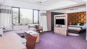 A modern hotel room with a sofa, a TV, a dining table, and a large window. - Shri Vitthal Mangalam (Satara)