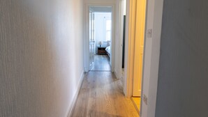 A narrow hallway with wooden flooring leading to a bedroom with a bed and a nightstand. - West Dartford Teal House (Dartford)