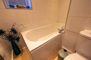A bathroom with a bathtub, toilet, and a window with a towel.