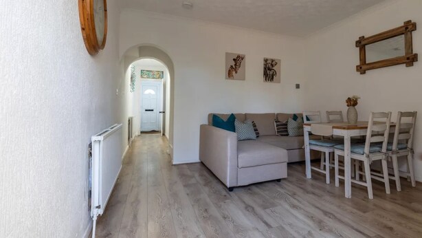 A spacious living area with a sofa, dining table, and chairs. A radiator is visible on the left, and a wooden-framed mirror hangs on the wall. - West Dartford Teal House (Dartford)