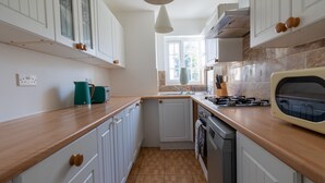 A kitchen with white cabinets, a wooden countertop, a vintage stove, and a window providing natural light. - West Dartford Teal House (Dartford)