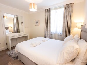 Une chambre d’hôtel avec un lit, une table de chevet, un miroir, une fenêtre avec des rideaux et une lampe.