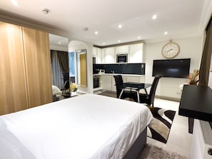 Una habitación de hotel moderna con una cama grande, una kitchenette pequeña, un comedor y un televisor montado en la pared.