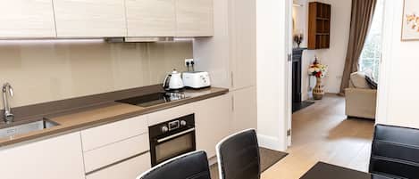 Une cuisine moderne avec des meubles en bois clair, un plan de travail noir et un coin repas comprenant des chaises noires et une table en verre.