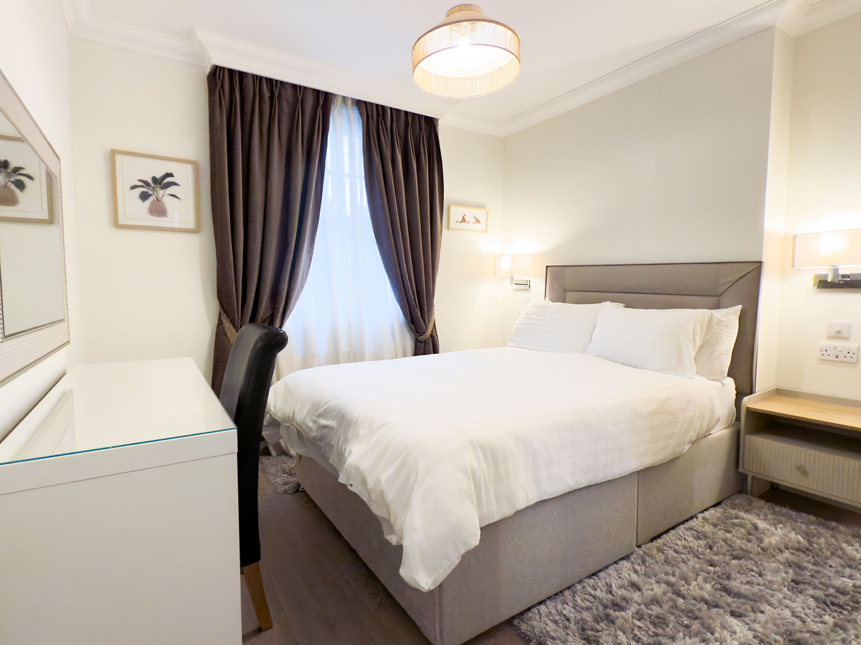 A hotel room with a bed, bedside table, chair, and a desk.