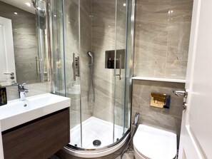 Un baño moderno con cabina de ducha de vidrio, lavamanos blanco y un inodoro.