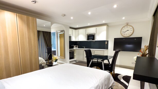 Una habitación de hotel moderna con una cama grande, una kitchenette pequeña, un comedor y un televisor montado en la pared.
