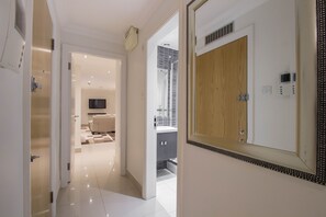 Un couloir d’hôtel moderne avec une porte en bois, un grand miroir et un téléviseur en arrière-plan.