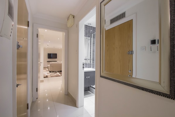 A modern hotel hallway with a wooden door, a large mirror, and a television in the background.