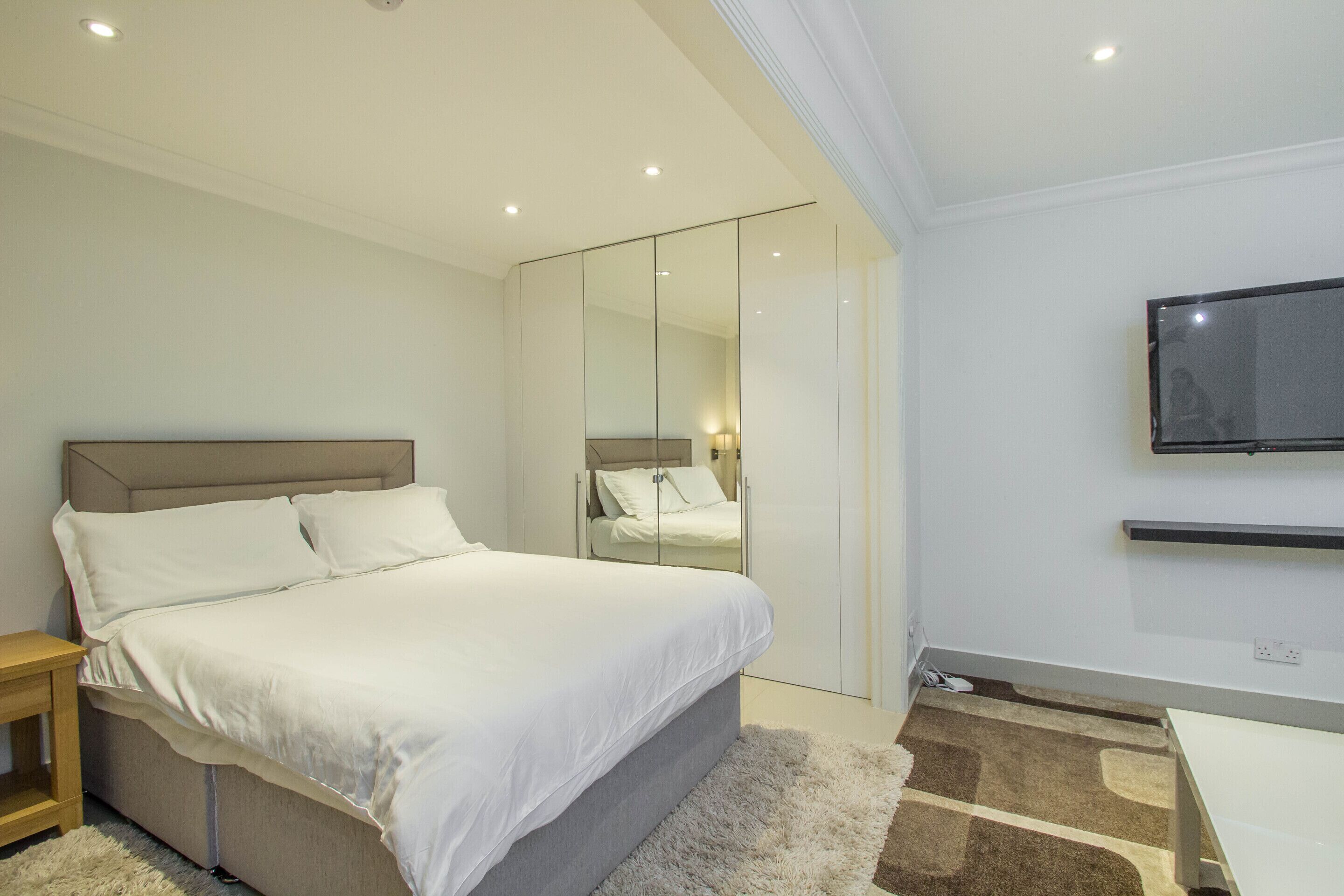 A modern bedroom with a bed, a TV mounted on the wall, and a wardrobe with a mirror.