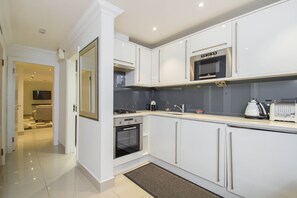 A modern kitchen with white cabinetry, a built-in oven, a microwave, and a coffee maker. - Spacious apartment for 4 (London)